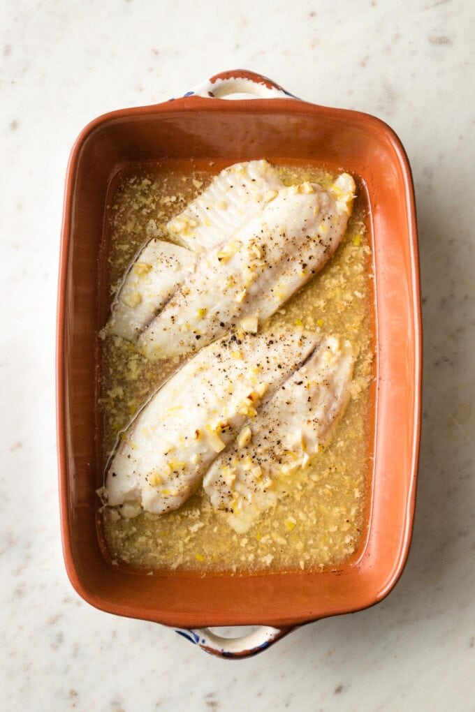 Baked tilapia with lemon butter sauce in pan.