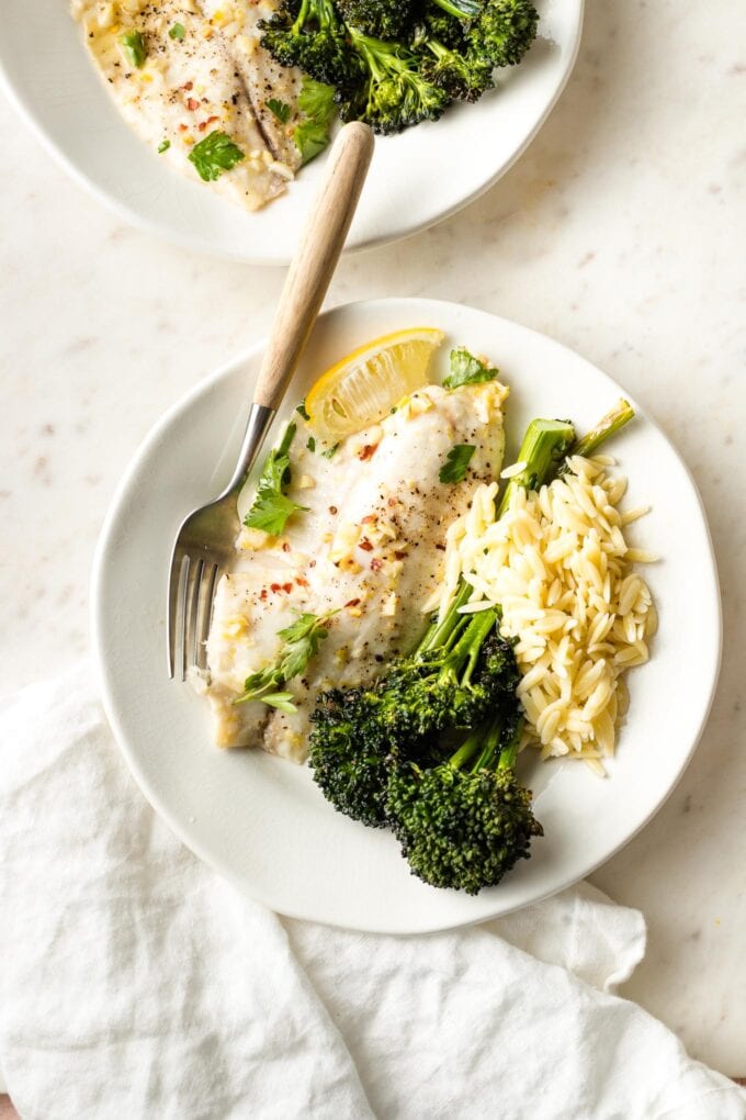 Baked tilapia filet plated with orzo and roasted broccolini.