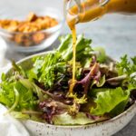 Dressing being poured on salad greens.