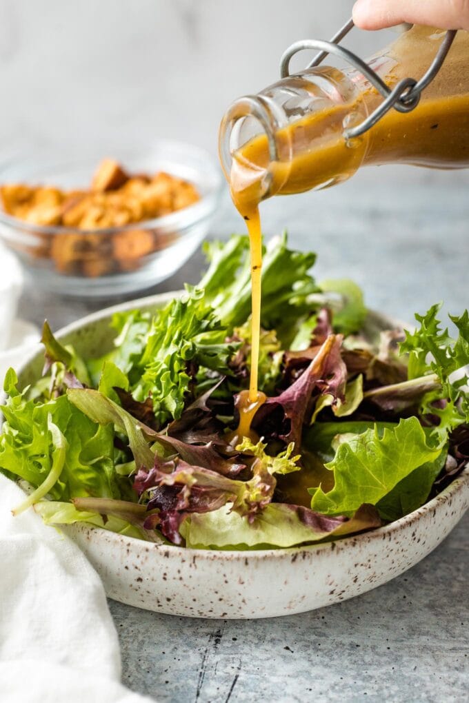 Dressing being poured on salad greens.