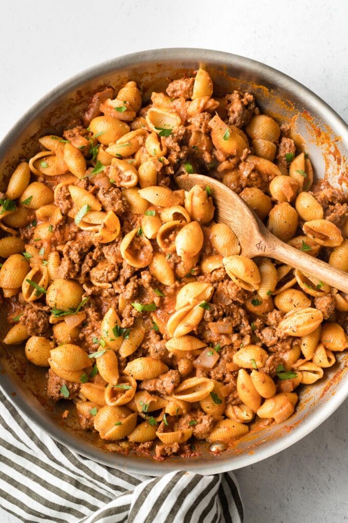 A skillet full of beef and shells seasoned with chili powder and garlic.