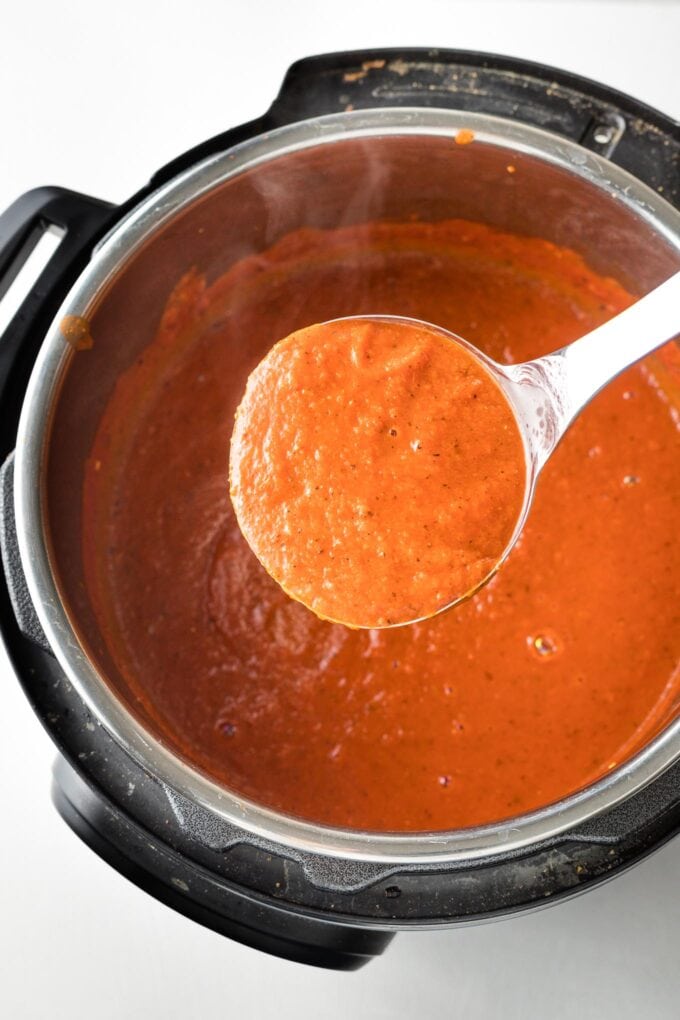 Ladle of smooth tomato soup held over full batch of soup in the bowl of an Instant Pot.