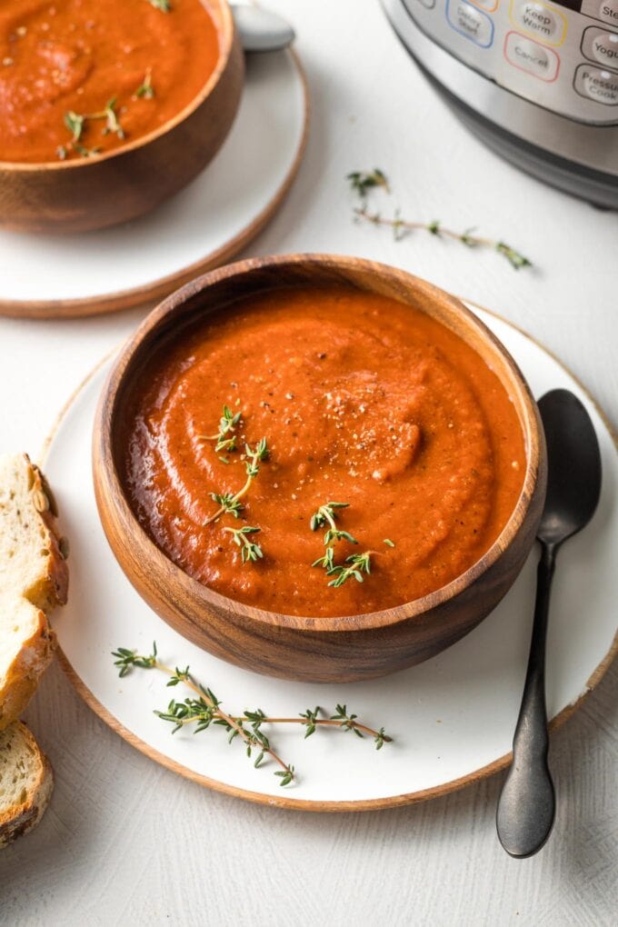 Instant Pot tomato soup served in a small wooden bowl with a garnish of fresh thyme.