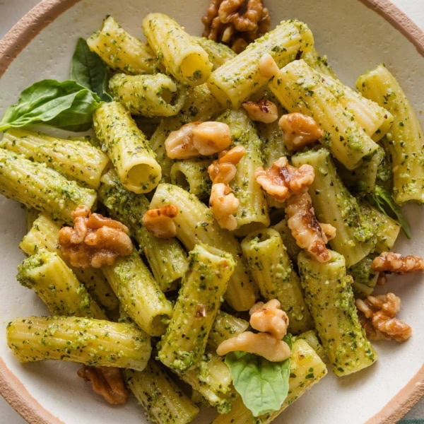 Close up of pesto rigatoni in a bowl topped with Parmesan and toasted walnuts.