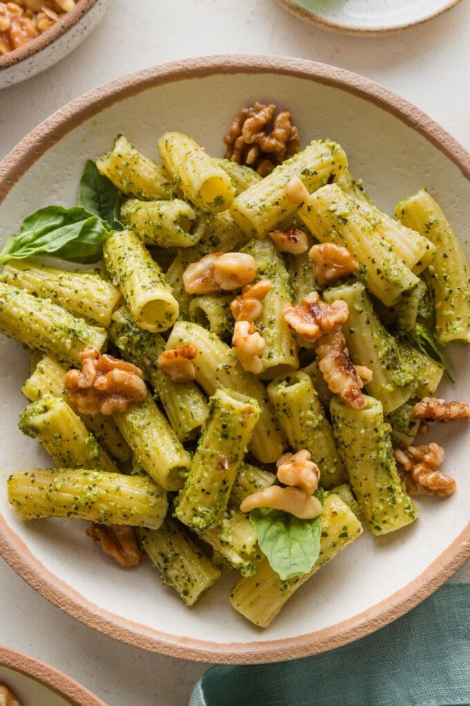 Close up of pesto rigatoni in a bowl topped with Parmesan and toasted walnuts.