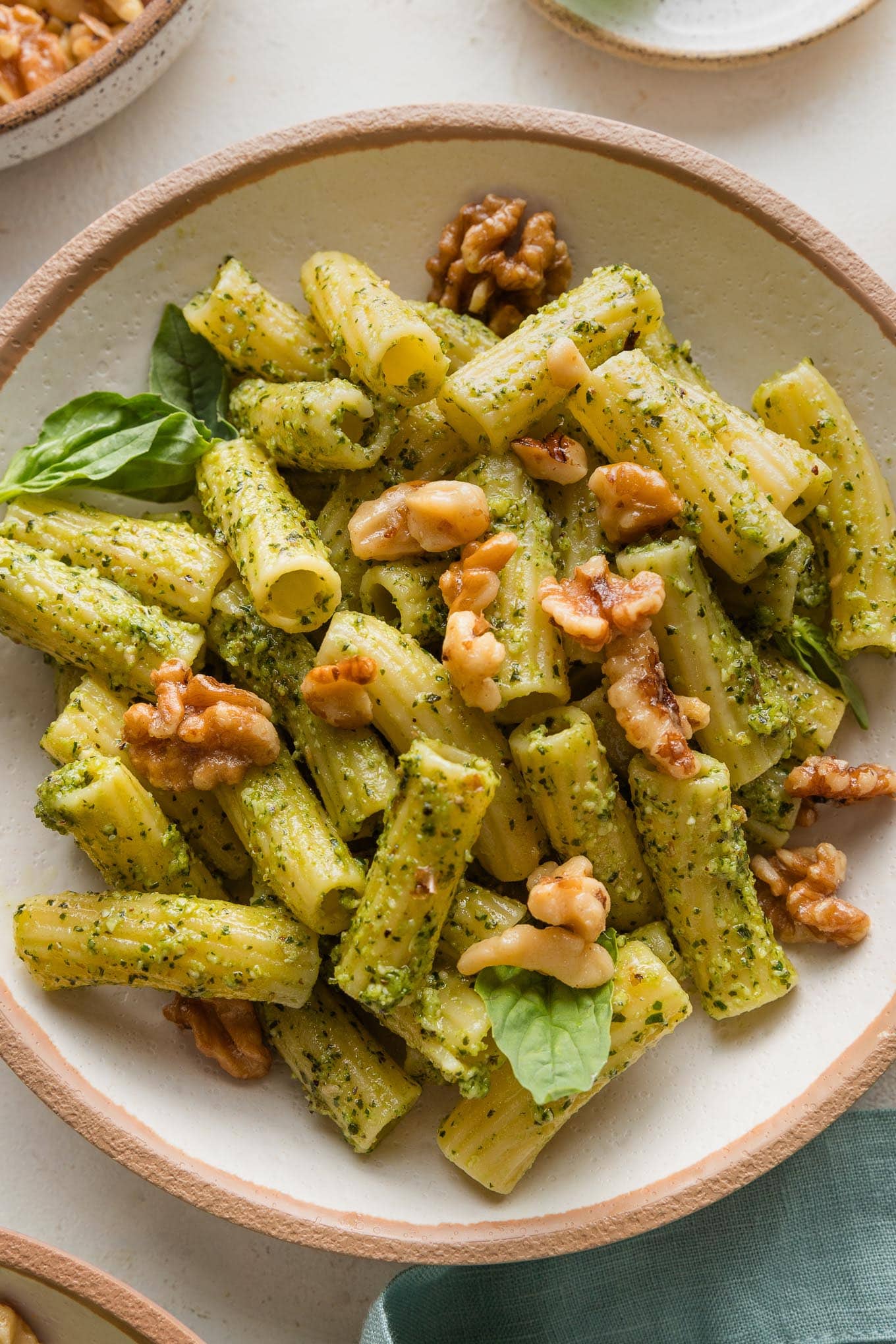 Close up of pesto rigatoni in a bowl topped with Parmesan and toasted walnuts.