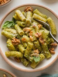 Fork scooping up a portion of pesto rigatoni with toasted walnuts on top.