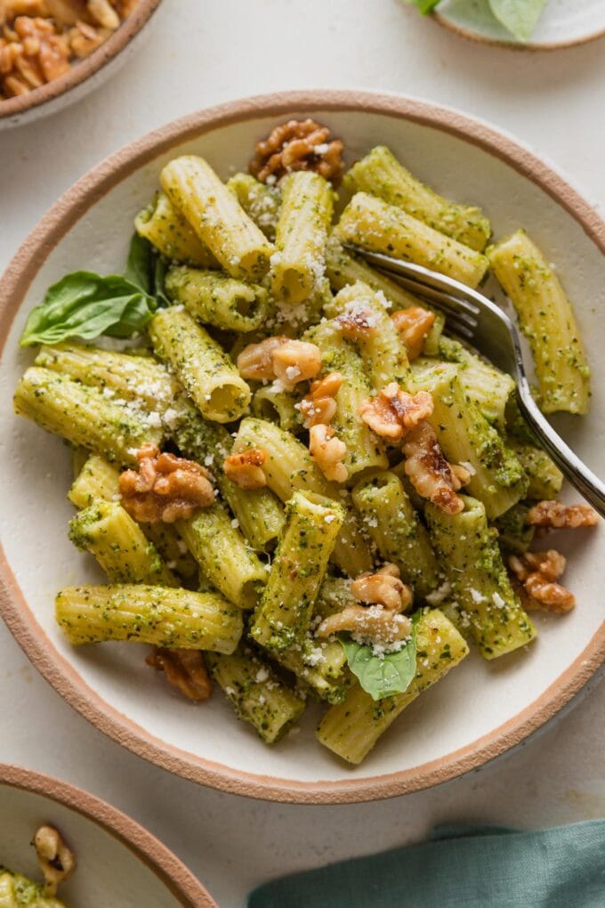 Fork scooping up a portion of pesto rigatoni with toasted walnuts on top.