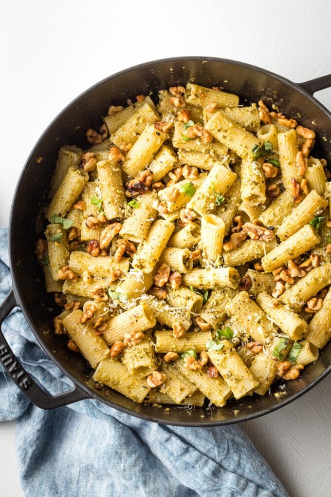 Deep cast iron skillet full of pesto rigatoni with Parmesan cheese on top.