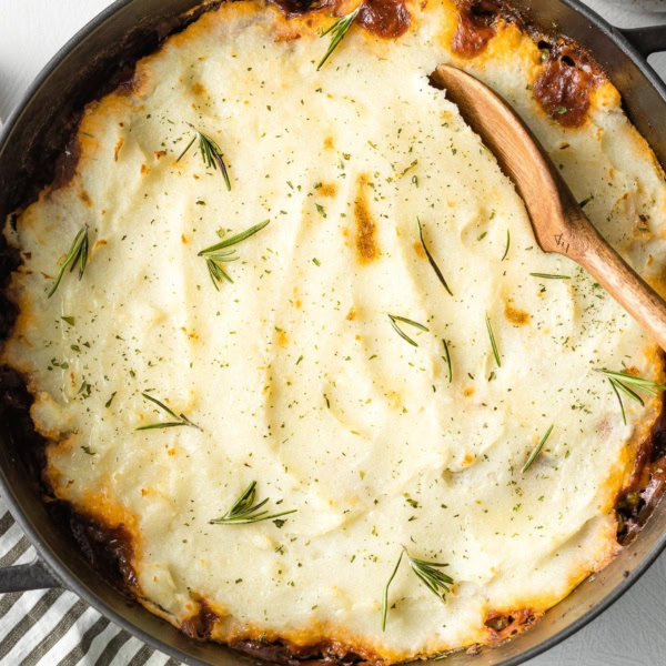 Wooden spoon about to lift out a serving of vegetarian Shepherd's pie from a deep cast iron skillet.