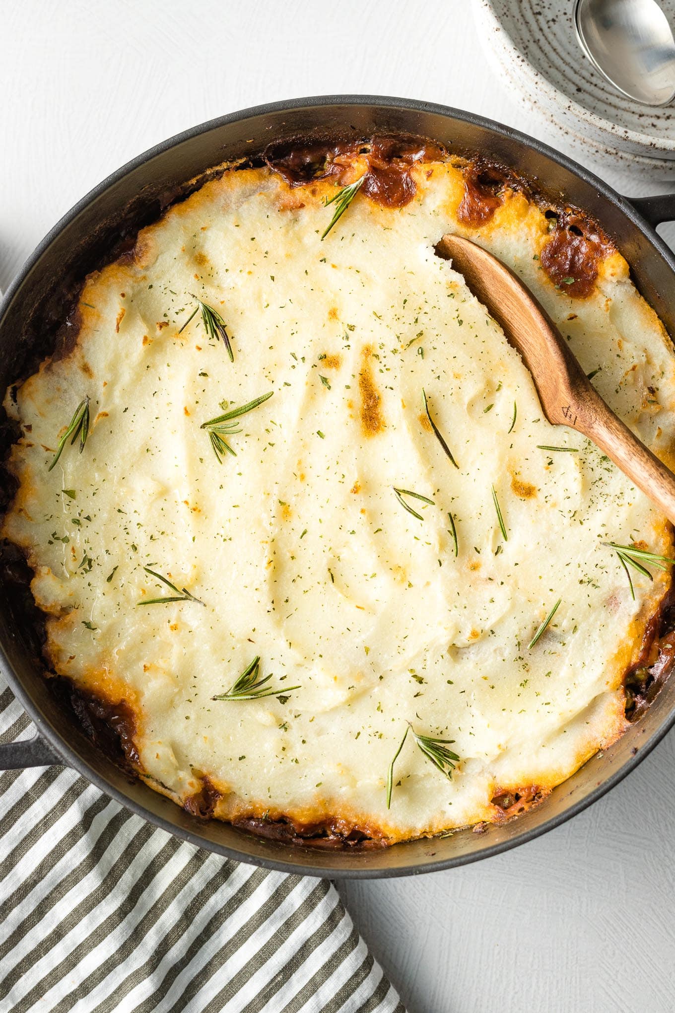 Wooden spoon about to lift out a serving of vegetarian Shepherd's pie from a deep cast iron skillet.