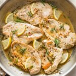 A skillet filled with lemon rosemary flavored chicken breasts in a white wine pan sauce.