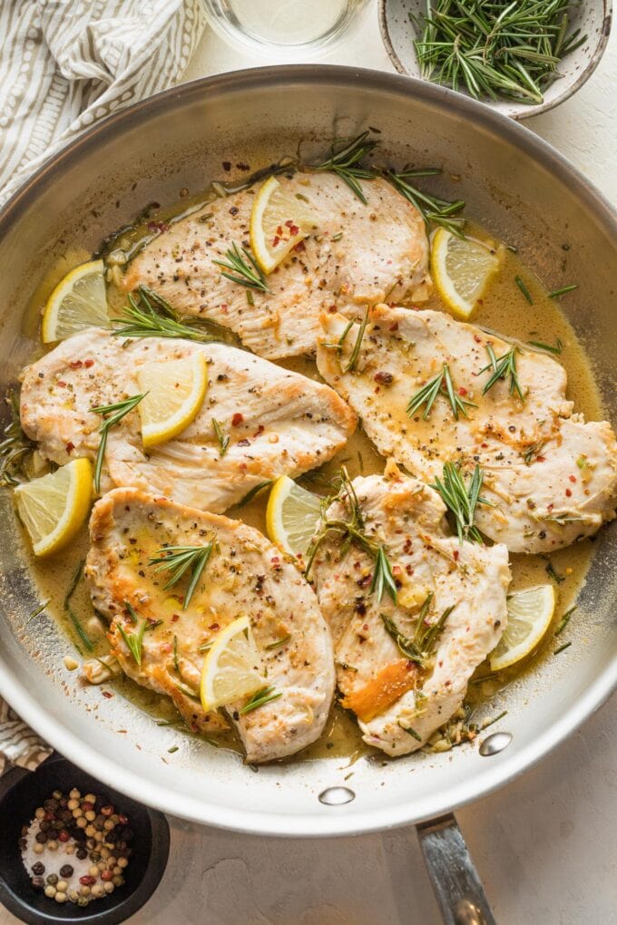 A skillet filled with lemon rosemary flavored chicken breasts in a white wine pan sauce.