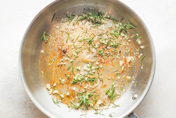 Step one of a recipe for lemon rosemary chicken: frying garlic and rosemary leaves in a skillet.