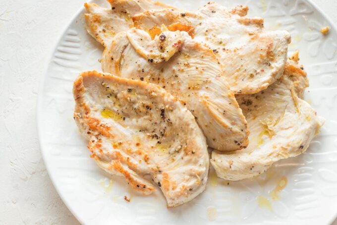 Lightly pan fried thin sliced chicken breasts removed to a white plate.