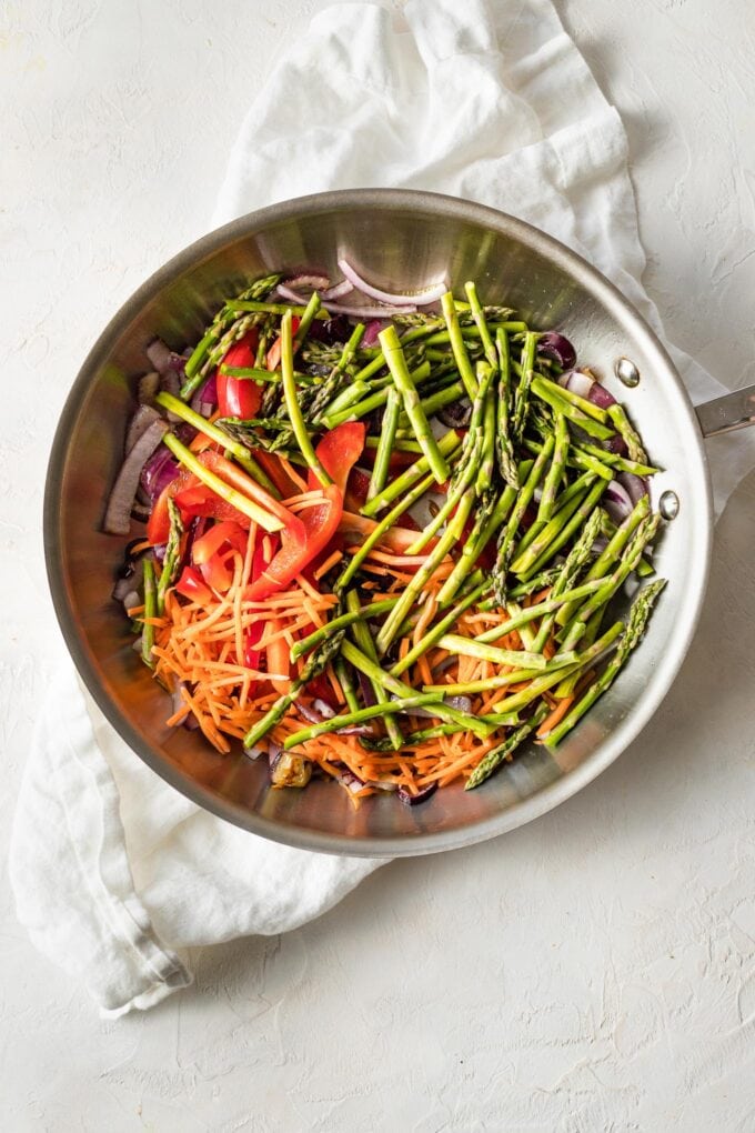 Skillet with asparagus, bell pepper, carrots, and red onion ready to cook.