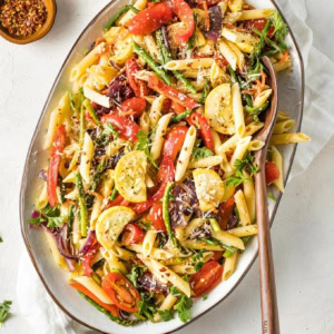 Large plate filled with a lemon herb pasta primavera and a wooden serving spoon.