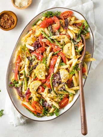 Large plate filled with a lemon herb pasta primavera and a wooden serving spoon.