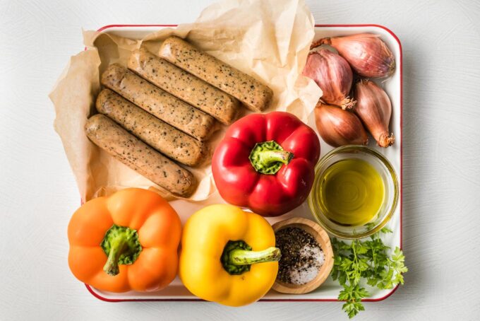 Tray with Italian-flavored chicken sausage links, three whole bell peppers, several whole shallots, herbs, olive oil, salt, pepper, and Italian seasoning.