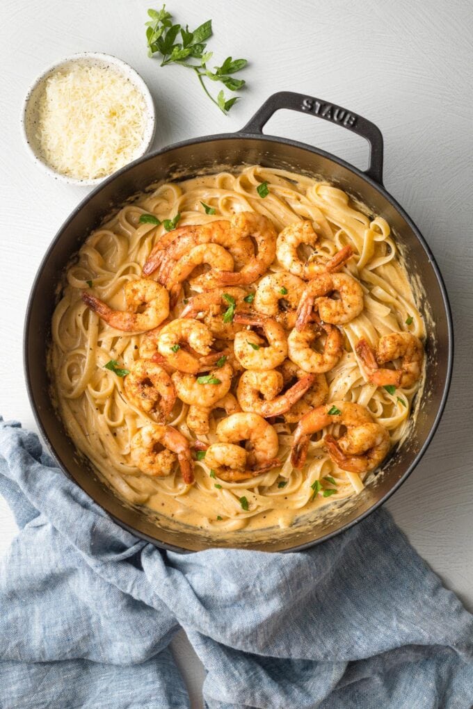Blackened shrimp piled on top of fettuccine pasta in creamy Alfredo sauce, in a black cast iron skillet.