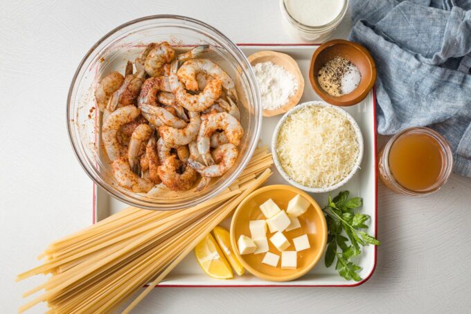 Shrimp with blackening seasoning, fettuccine, butter, Parmesan, flour, cream, broth, parsley, lemon, and seasonings arranged on a tray.
