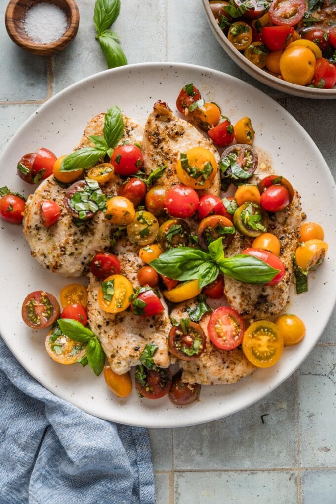 Platter of bruschetta-topped chicken breasts topped with extra fresh basil and resting on a countertop, ready to serve.
