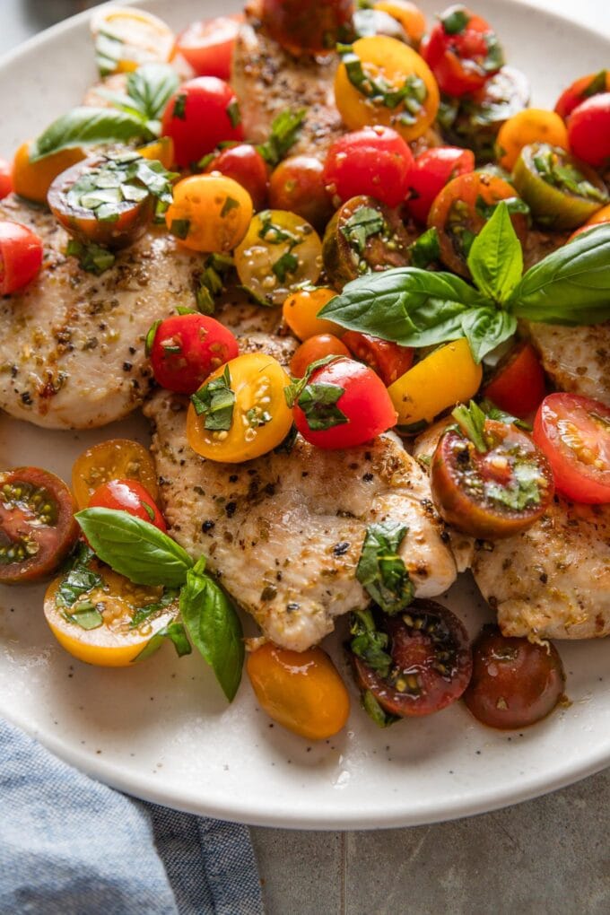 Close up view of bruschetta topped chicken breasts on a plate.