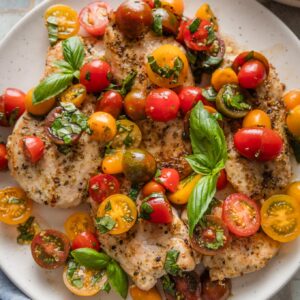 Platter filled with chicken breasts topped with tomato basil bruschetta.