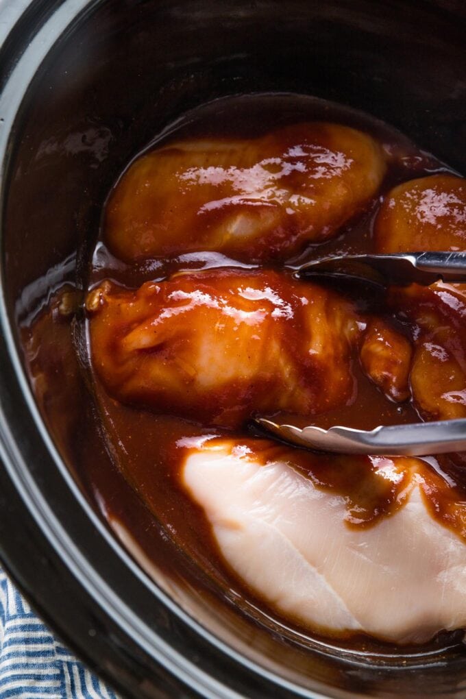 Chicken breasts nestled in BBQ sauce in the bowl of a slow cooker.