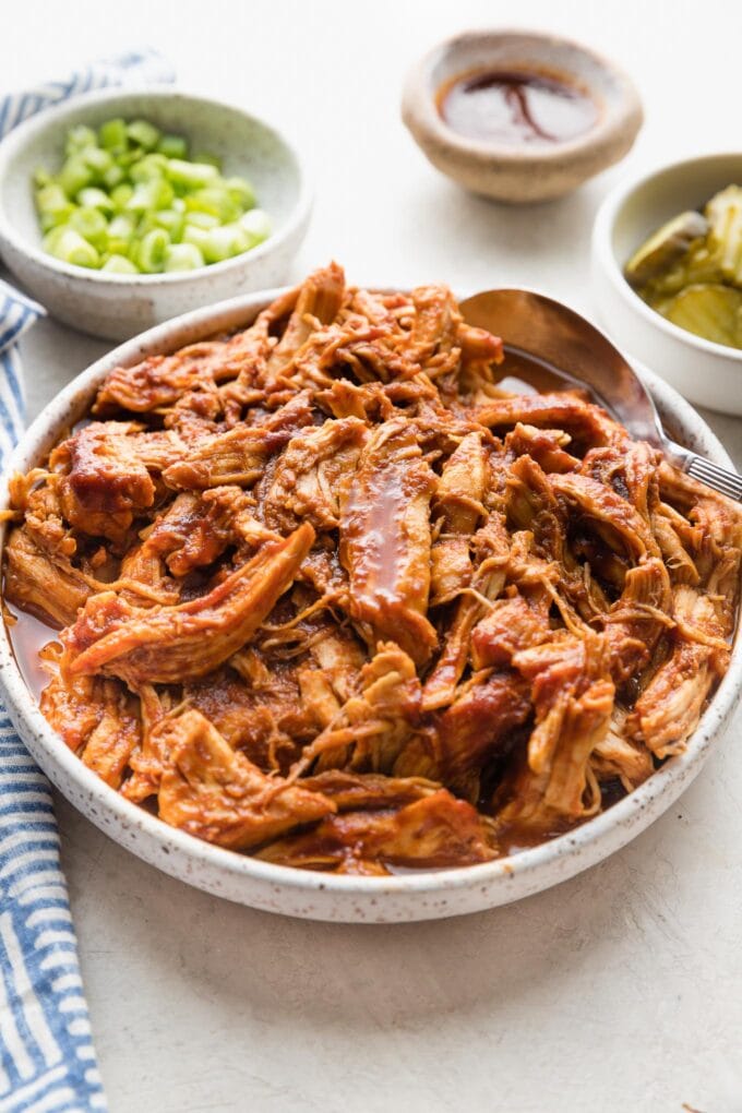 Angled view of a serving bowl full of BBQ pulled chicken made in a slow cooker.