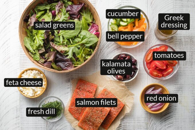 Salad greens, feta cheese, cucumber, chopped pepper, halved cherry tomatoes, Greek salad dressing, salmon filets, and olives in prep bowls.