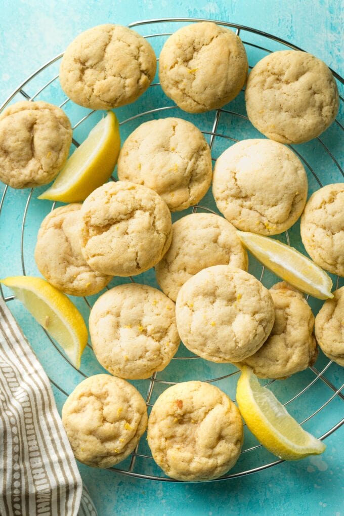 Wire rack piled high with soft lemon sugar cookies on a blue background.