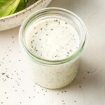 Small jar of dressing with salad greens in the background.