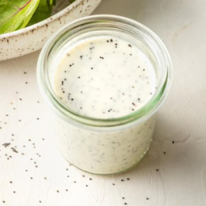 Small jar of dressing with salad greens in the background.