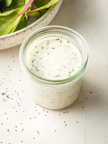 Small jar of dressing with salad greens in the background.
