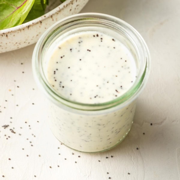 Small jar of dressing with salad greens in the background.