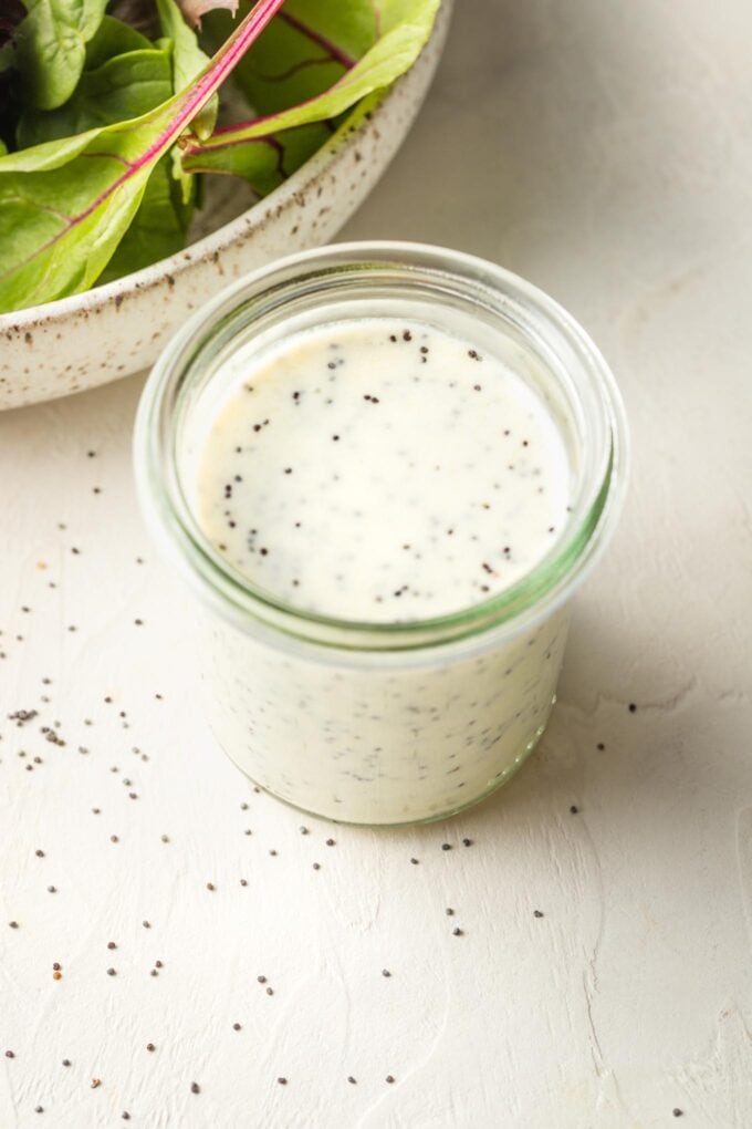 Small jar of dressing with salad greens in the background.
