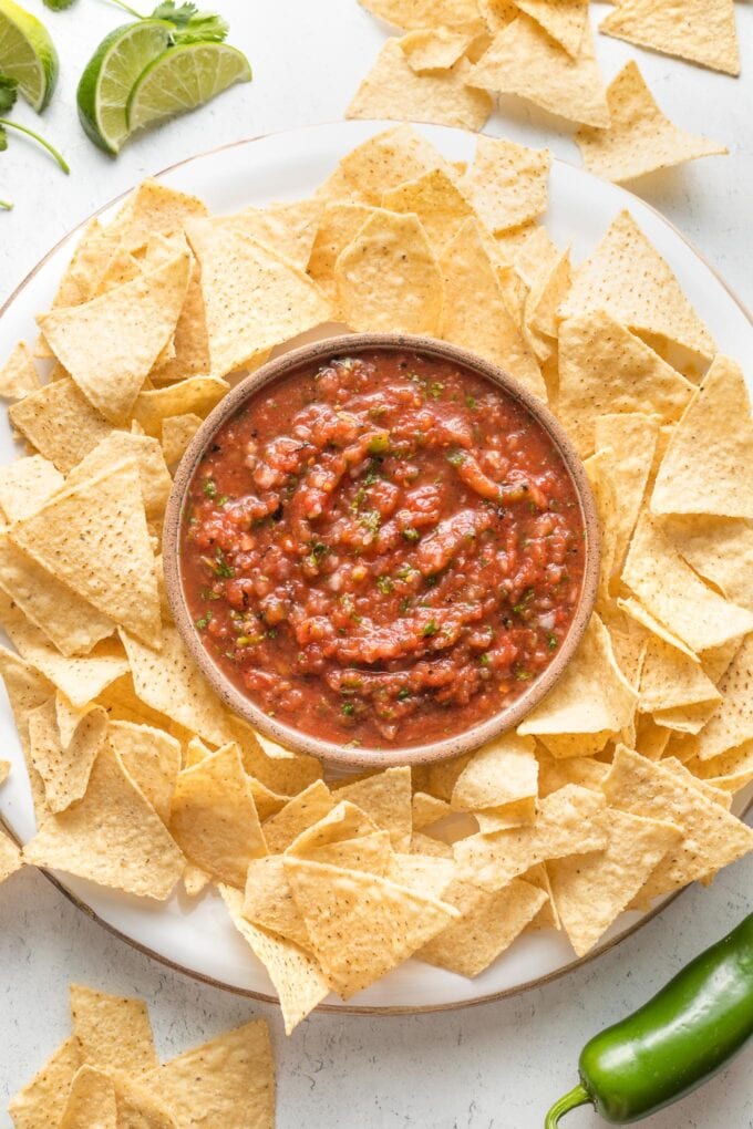Bowl of blender salsa on a tray surrounded by tortilla chips.