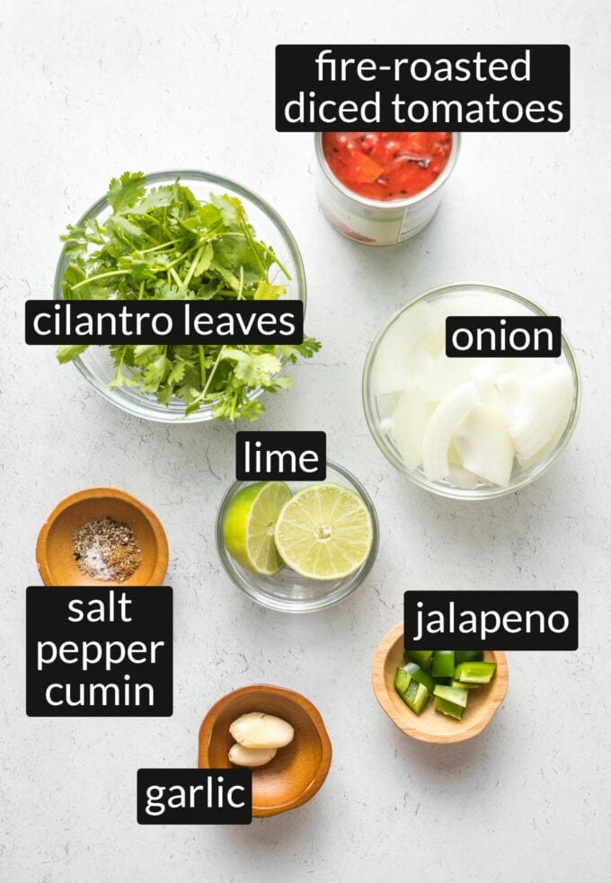 Can of fire-roasted tomatoes, bowls with cilantro, onion, limes, garlic, jalapeno, salt, pepper, and cumin.