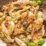 Skillet with cooked chicken breasts, sun-dried tomatoes, and artichokes in a light cream sauce, garnished with basil.