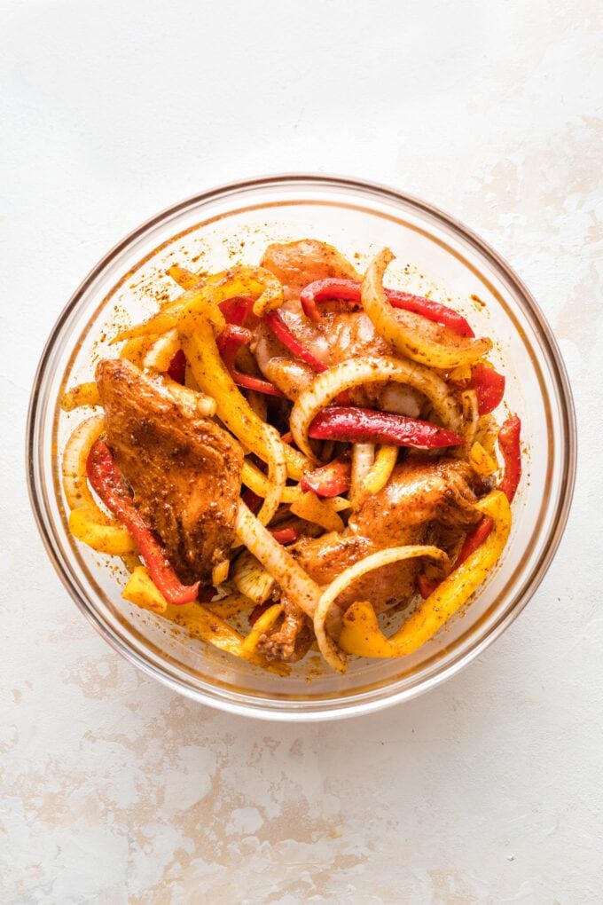 Chicken breasts and sliced peppers and onions marinating in fajita seasoning.