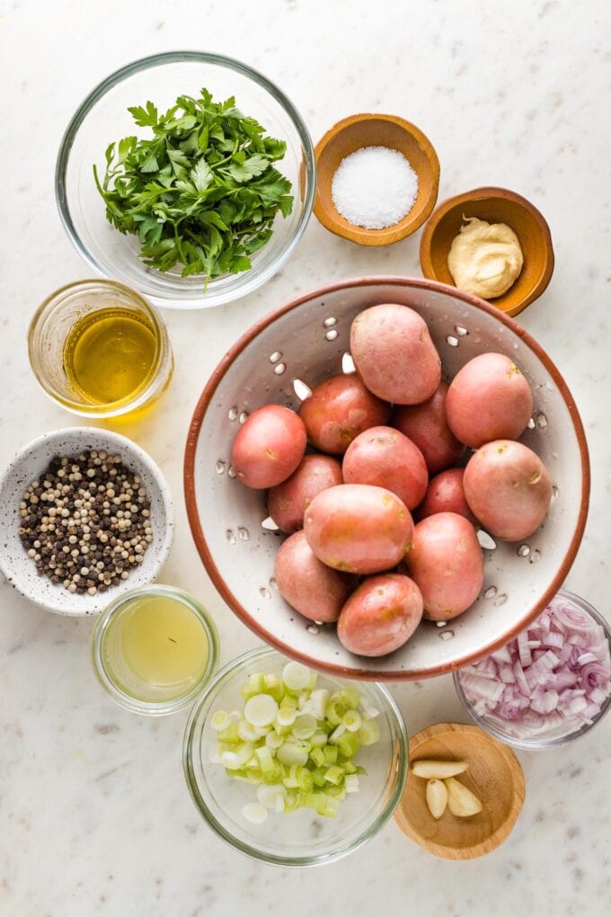 Bowls with washed red potatoes, fresh herbs, peppercorns, lemon juice, green onions, garlic, and shallots.