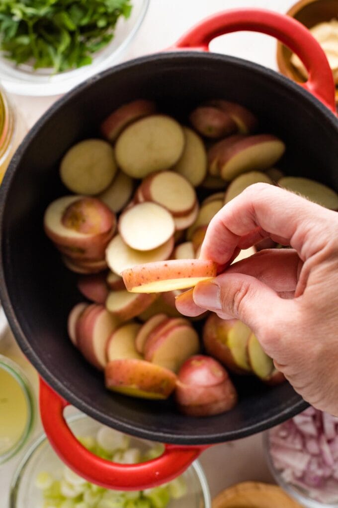 Close-up of a hand holding a sliced potato to show it's about 1/4" thick.