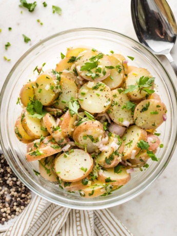 Potato salad in a serving bowl, surrounded by extra garnish.