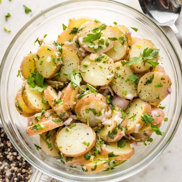 Potato salad in a serving bowl, surrounded by extra garnish.