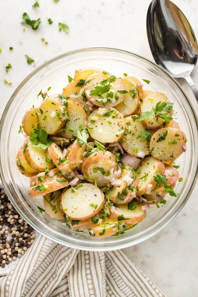 Potato salad in a serving bowl, surrounded by extra garnish.