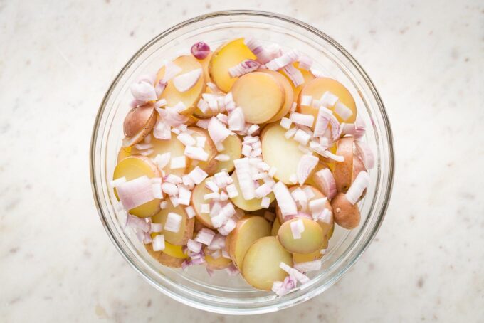 Cooked potatoes drained and transferred to a serving bowl, sprinkled with shallots.