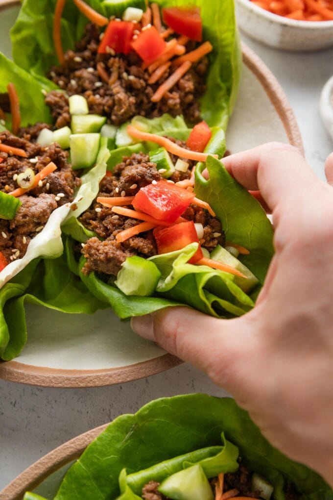 A woman's hand picking up a lettuce wrap from a plate.