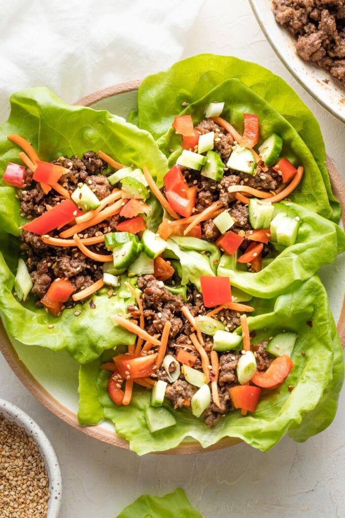 Three Korean beef lettuce wraps piled into a white bowl, ready to eat.