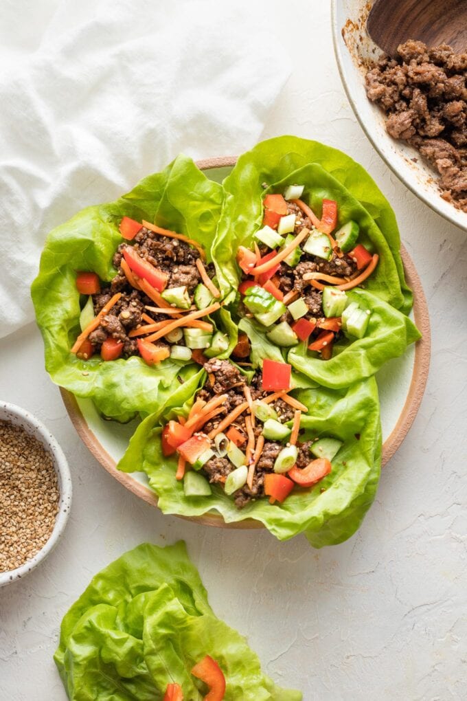 Bowl with three lettuce wraps surrounded by extra Korean ground beef, lettuce cups, and sesame seeds.